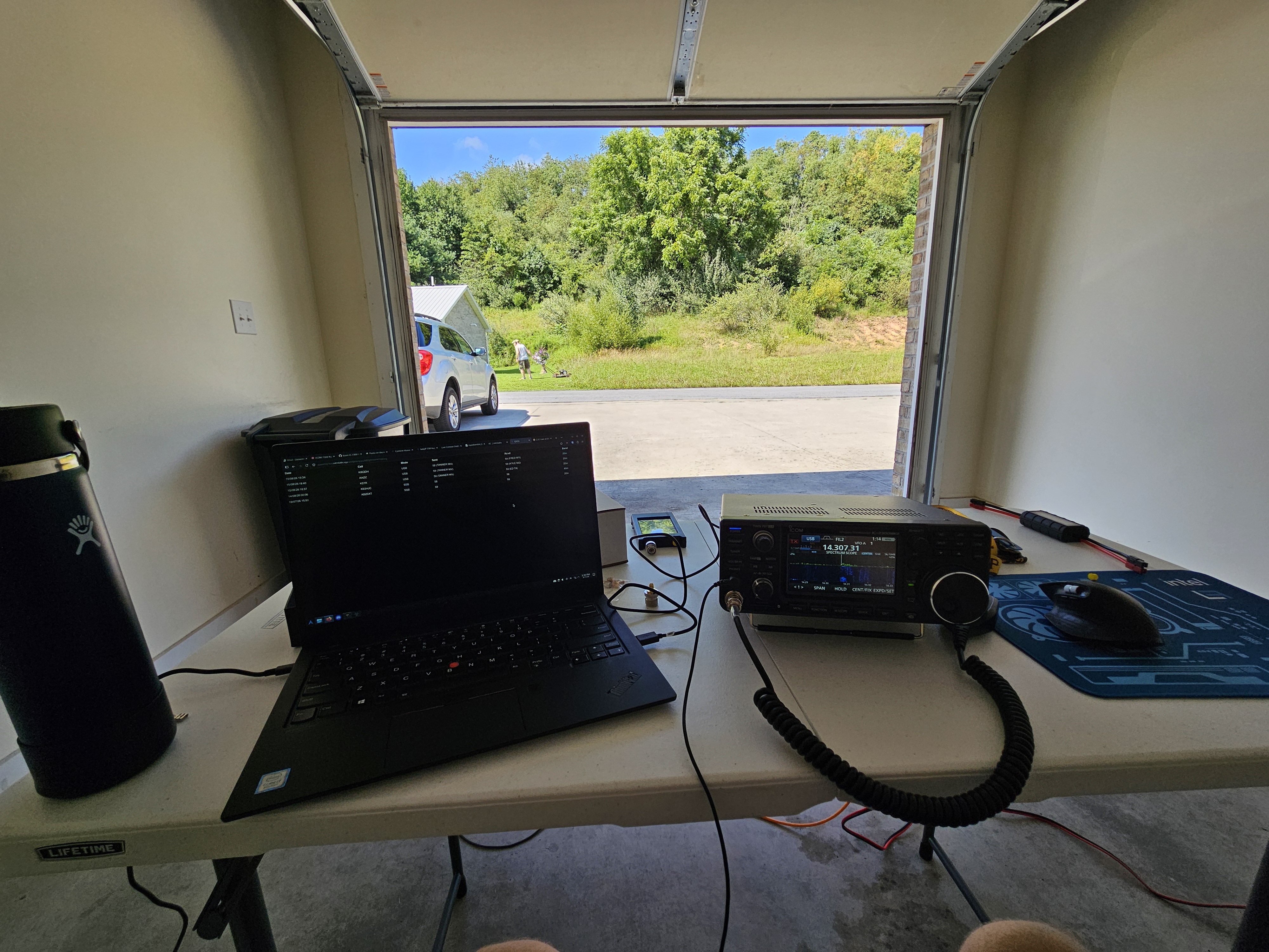 A laptop and Icom IC-7300 Mk2 amateur radio sit on a folding table inside an open one car garage